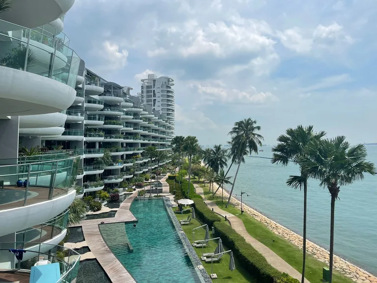 Seascape, photograph: the pool, timber decks and the lawn along the shoreline promenade seen from an upper balcony, with palms, the rock edge of the shore and the open sea